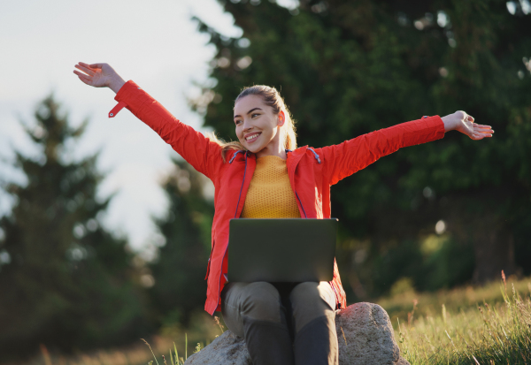 Front view of happy young woman using laptop in summer nature, outdoor office concept.