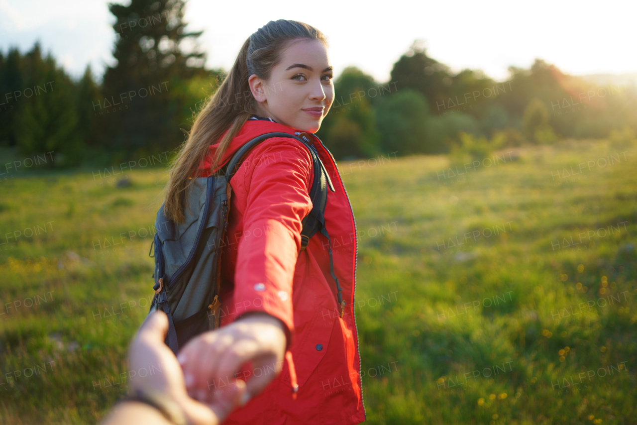 Happy young woman with backpack in summer nature, looking over shoulder at unrecognizable man.