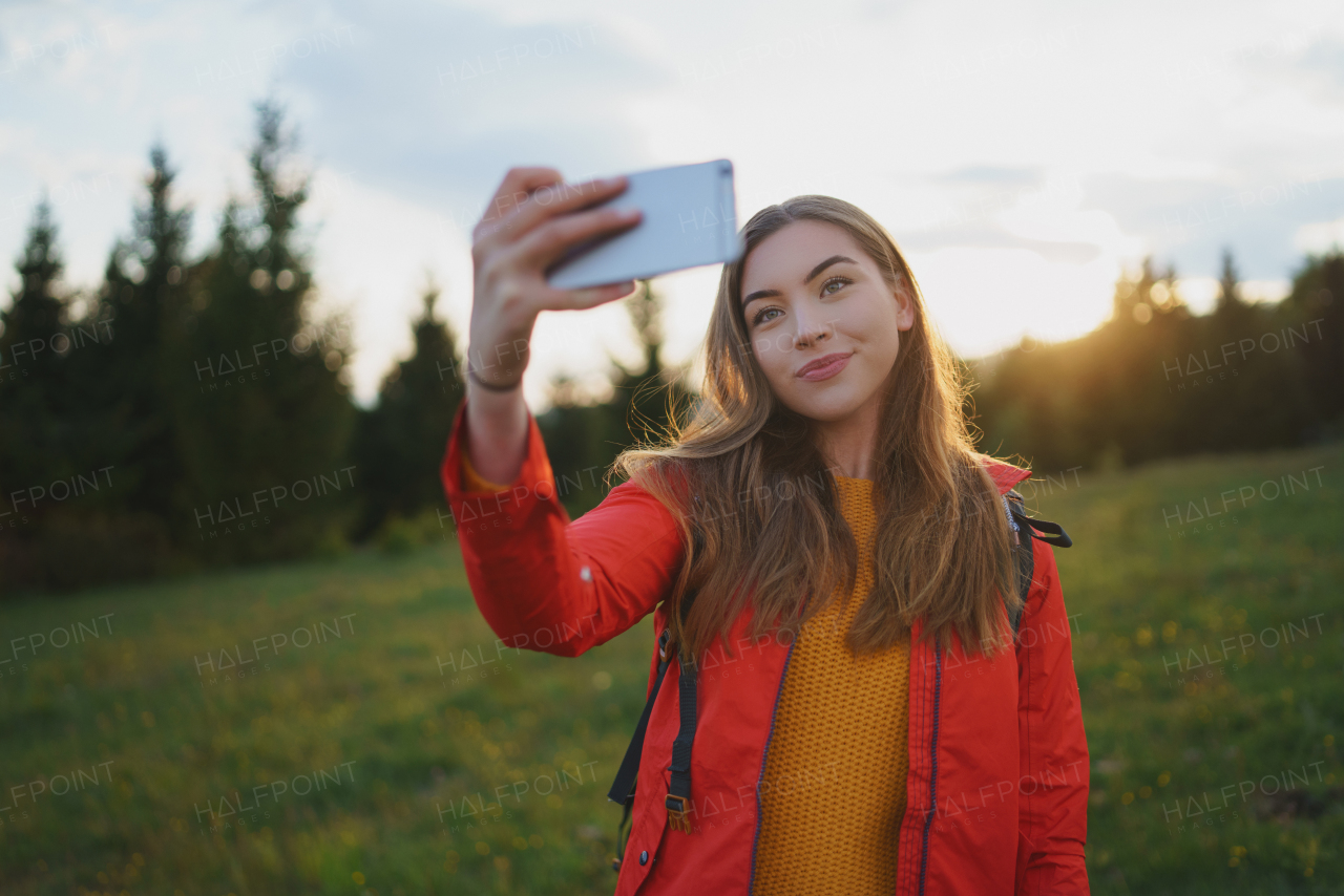 Side view of young woman on a walk outdoors on meadow in summer nature, taking selfie.