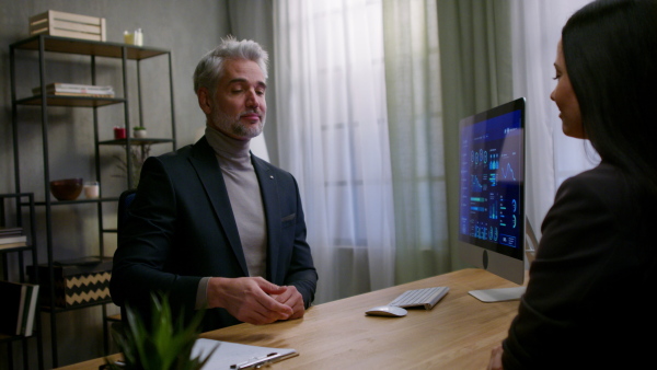 A mature financial advisor consulting with his client indoors in office, shaking hand.