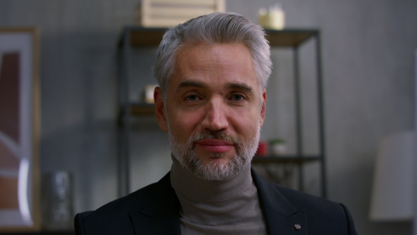 A close up of mature businessman indoors in office, looking at camera.