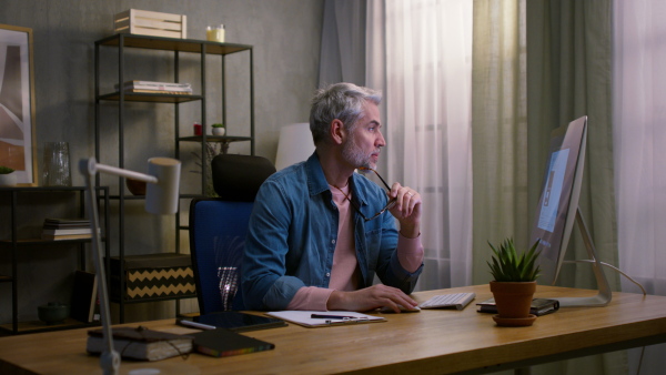 A mature man architect working on computer at desk indoors in office.