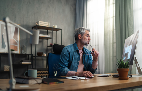 A mature man architect working on computer at desk indoors in office.