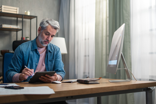 A mature man architect working on computer at desk indoors in office.