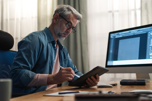 A mature man architect working on computer at desk indoors in office.