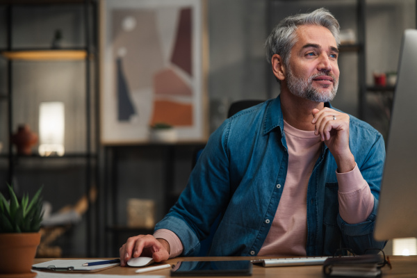 A mature man architect working on computer at desk indoors in office.