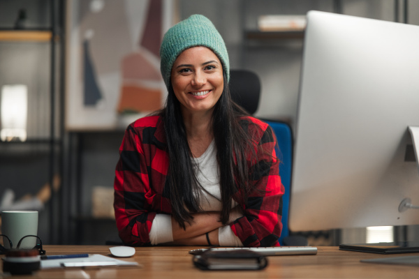 A happy female video editor works indoors in creative office studio, looking at camera.