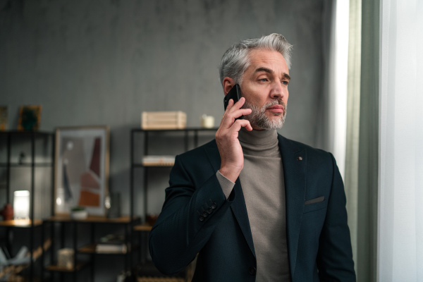 A mature businessman making a phone call indoors in office, looking away.