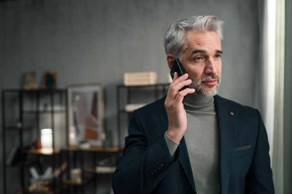 A mature businessman making a phone call indoors in office, looking away.