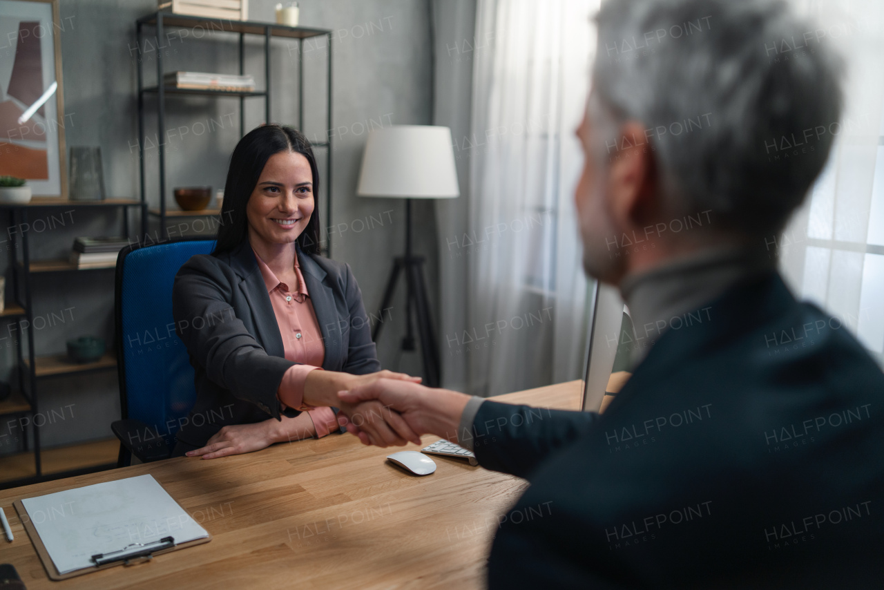 A financial advisor shaking hand with her client indoors in office.