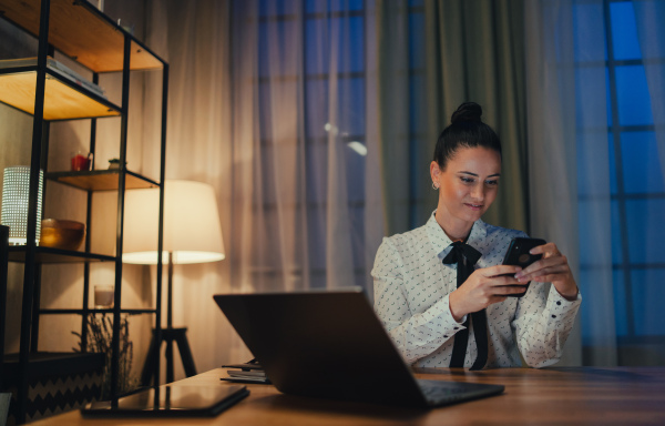 A happy mid adult business woman with diary working on laptop in office at night, looking at camera.