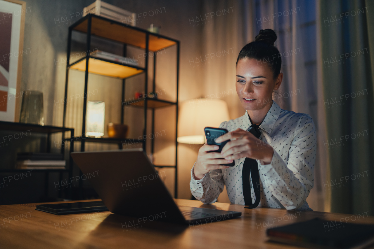 A happy mid adult business woman with diary working on laptop in office at night, looking at camera.