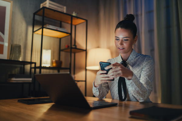 A happy mid adult business woman with diary working on laptop in office at night, looking at camera.