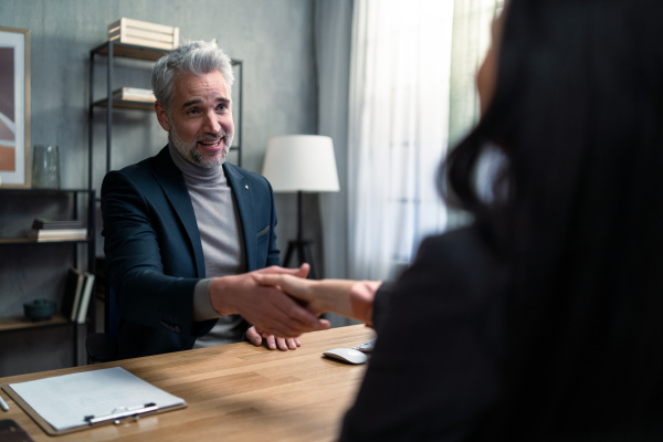 A mature financial advisor shaking hand with his client indoors in office.