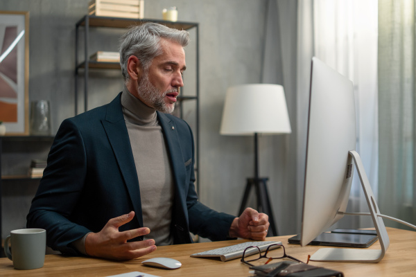 A mature businessman indoors in office, having video call.