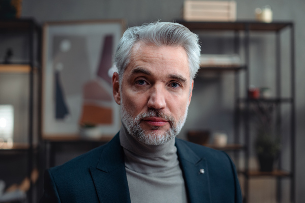 A close up of mature businessman indoors in office, looking at camera.