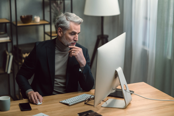 A mature businessman working on computer indoors in office.