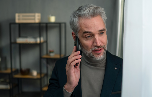 A mature businessman making a phone call indoors in office, looking away.