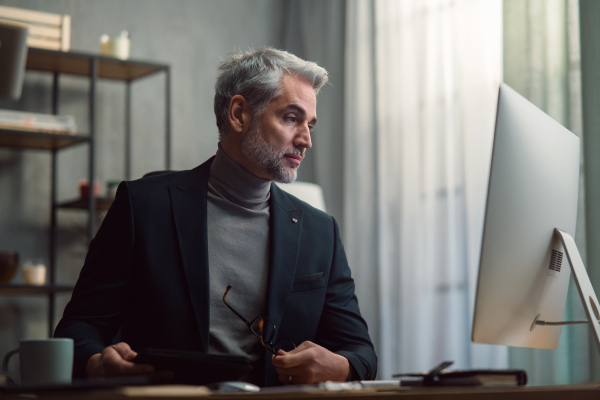 A mature businessman working on computer indoors in office.