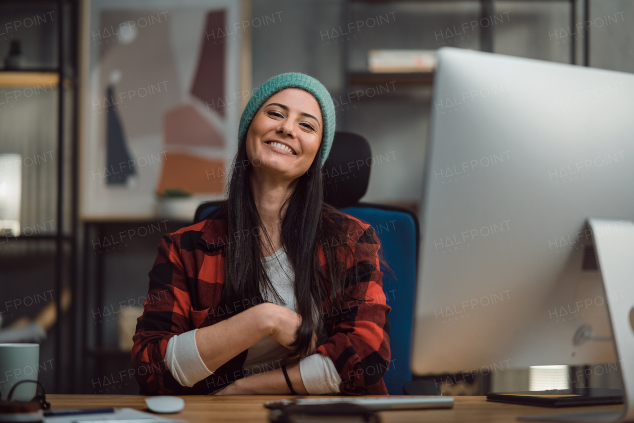 A happy female video editor works indoors in creative office studio, looking at camera.