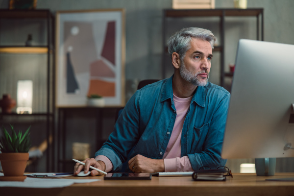 A mature man architect working on computer at desk indoors in office.