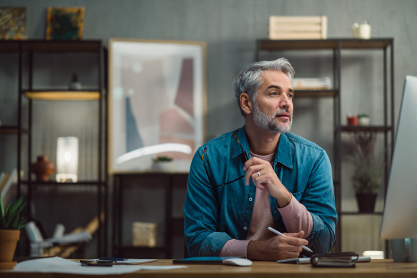 A mature man architect working on computer at desk indoors in office.