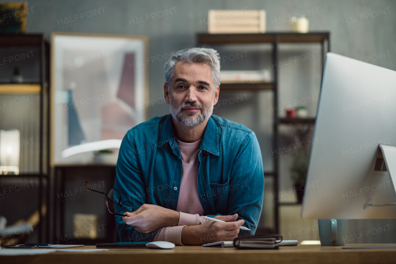 A mature man architect working on tablet at desk indoors in office, looking at camera.