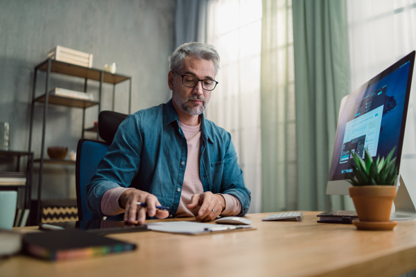 A mature man architect working on computer at desk indoors in office.