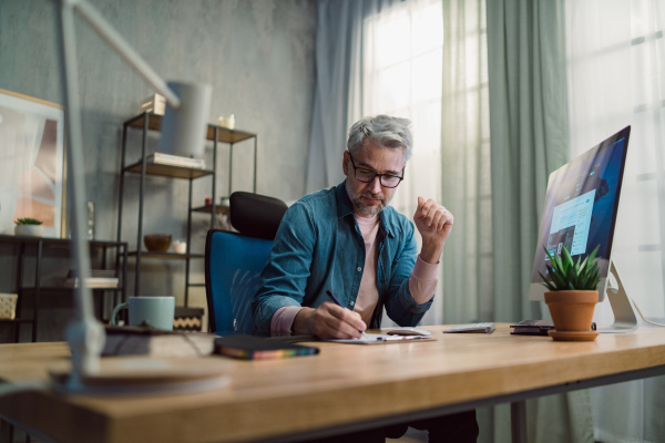 A mature man architect working on computer at desk indoors in office.