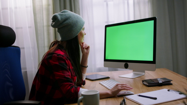 A mid adult hispter woman typing and working on computer indoors in creative office studio.