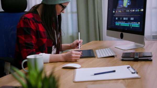 A female video editor works with footage on her personal computer indoors in creative office studio.