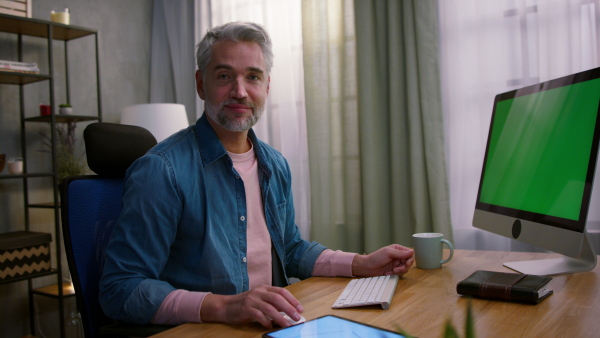 A mature man architect working on computer at desk indoors in office, looking at camera.