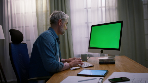 A mature man architect working on computer at desk indoors in office.