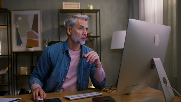 A mature man architect working on computer at desk indoors in office.