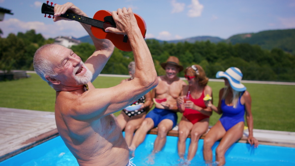 Group of cheerful seniors with guitar by swimming pool outdoors in backyard, a party concept.