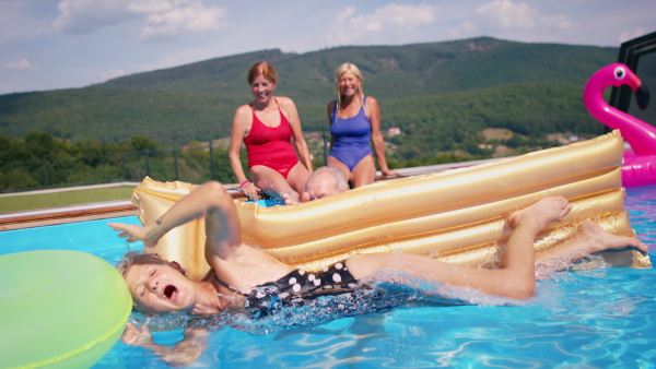 Group of cheerful seniors in swimming pool outdoors in backyard, having fun.