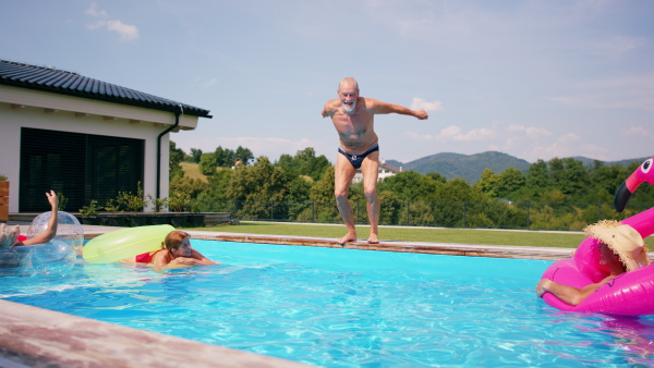 Group of cheerful seniors in swimming pool outdoors in backyard, jumping in water.