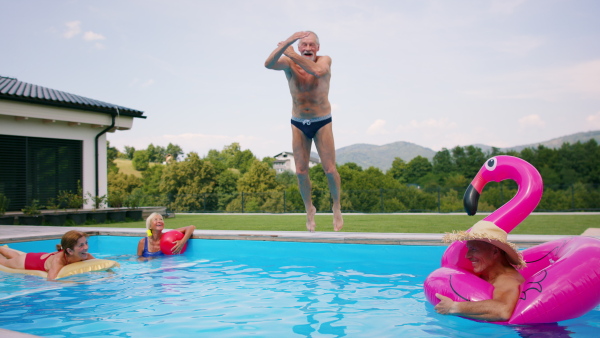 Group of cheerful seniors in swimming pool outdoors in backyard, jumping in water.