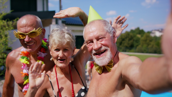 Group of cheerful seniors by swimming pool outdoors in backyard, a party concept.