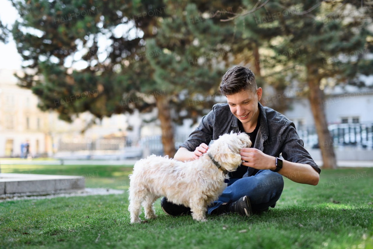 A portrait of young man with dog outdoors in city park, resting.