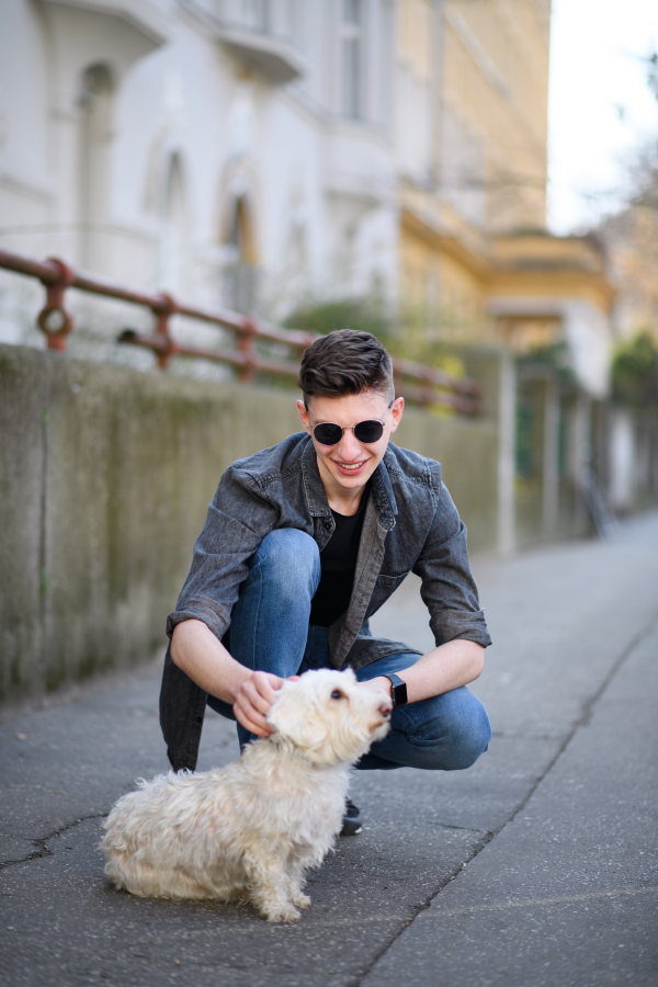 A portrait of happy young man with pet dog outdoors on street in city.