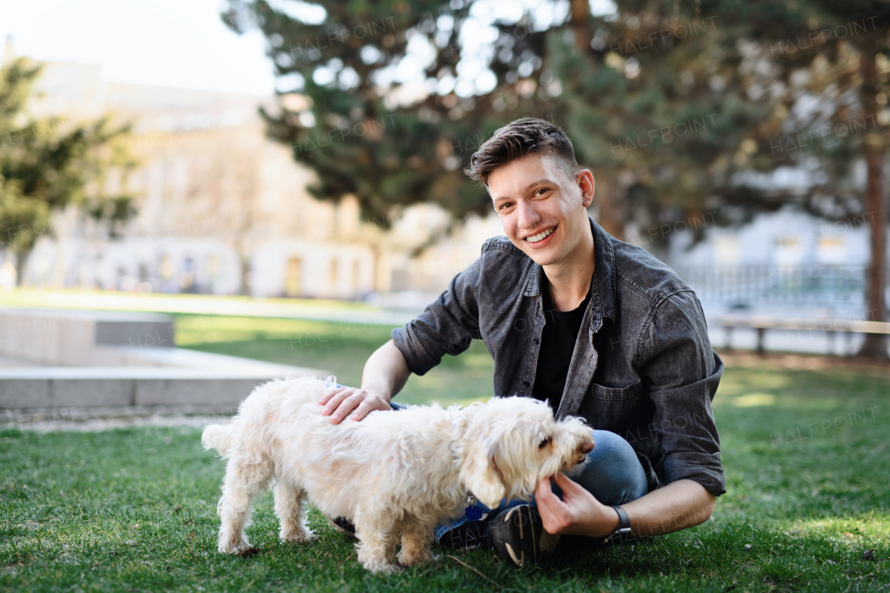 A portrait of young man with dog outdoors in city park, looking at camera.