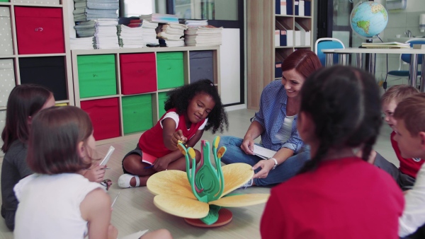 A group of small school kids with teacher sitting on the floor in class, learning science.