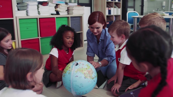 A group of small school kids with teacher sitting on the floor in class, learning geography.