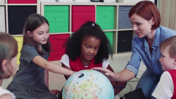 A group of small school kids with teacher sitting on the floor in class, learning geography.