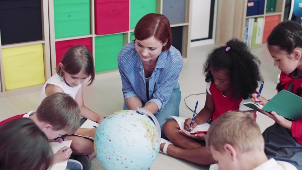 A group of small school kids with teacher sitting on the floor in class, learning geography.