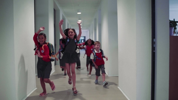 A group of cheerful small school kids in corridor, running. Back to school concept.