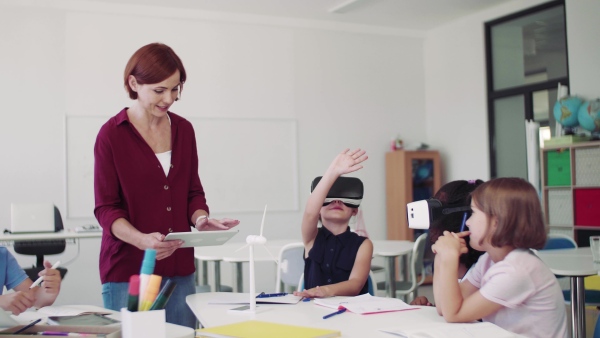 A group of small school kids with VR goggles and teacher in class, learning.