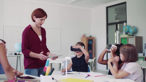 A group of small school kids with VR goggles and teacher in class, learning.