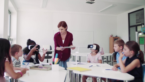 A group of small school kids with VR goggles and teacher in class, learning.